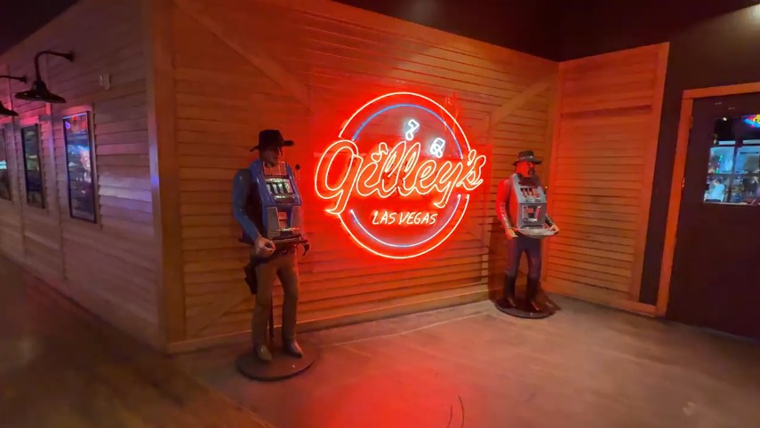 Exterior neon sign for Gilley's, with old school slot machines modeled as cowboys on either side.