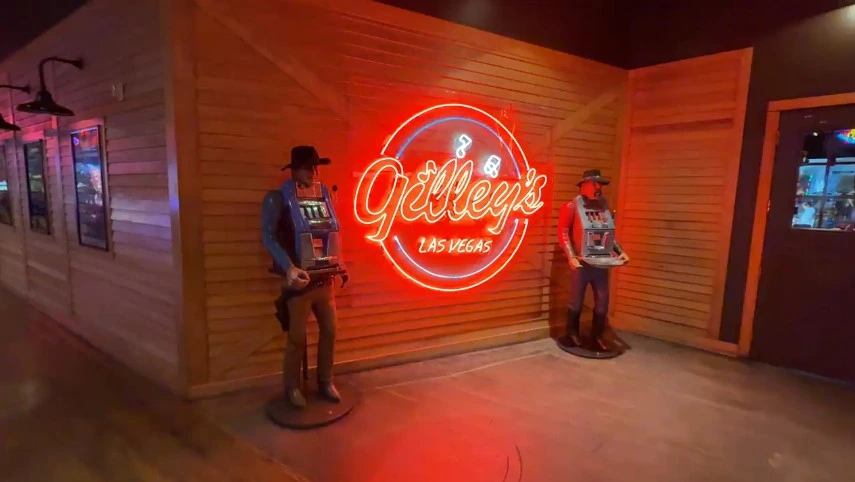 Exterior neon sign for Gilley's, with old school slot machines modeled as cowboys on either side. 