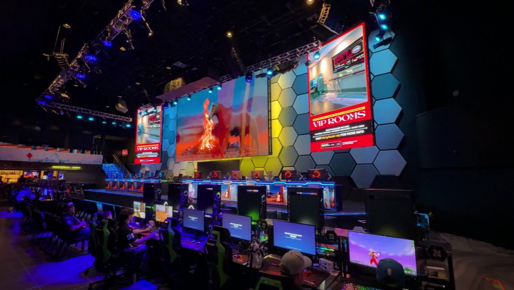 A massive screen with a bank of seats and gaming stations facing it.