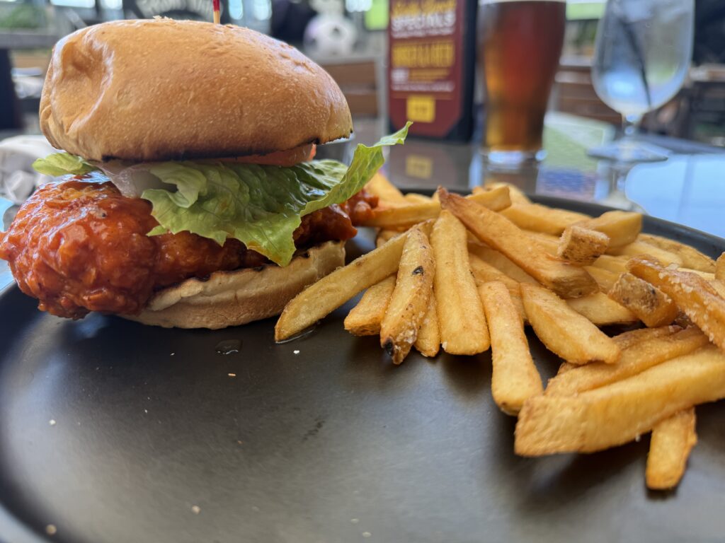 A buffalo chicken sandwich, plated next to a handful of french fries. 
