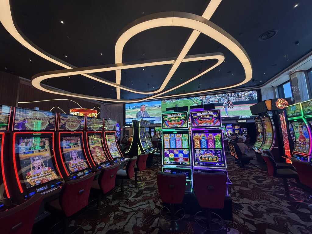 A new, modern looking section of the casino, which is packed iwth slot games and has a decorative light fixture on the ceiling overhead.