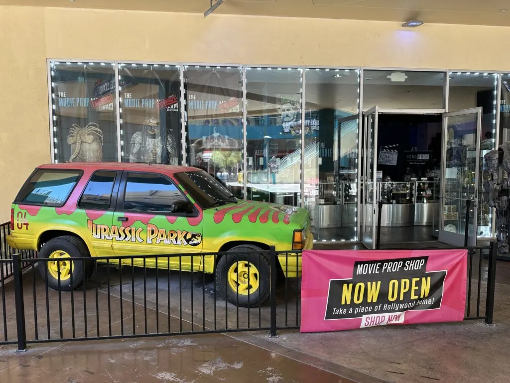 A tour vehicle from the movie Jurassic Park sits in front of the Movie Prop Experience.