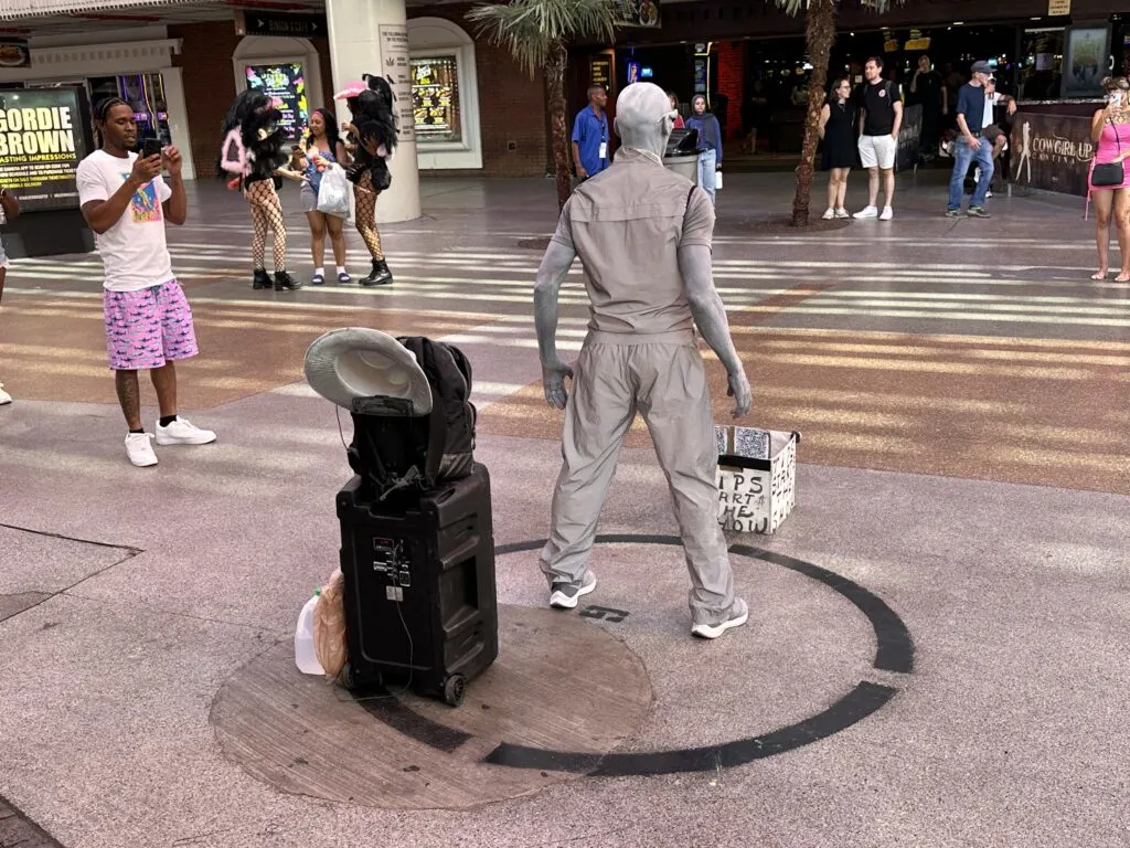 A street perormer dressed in gray and with skin painted in gray poses, waiting for a tip to start the show.