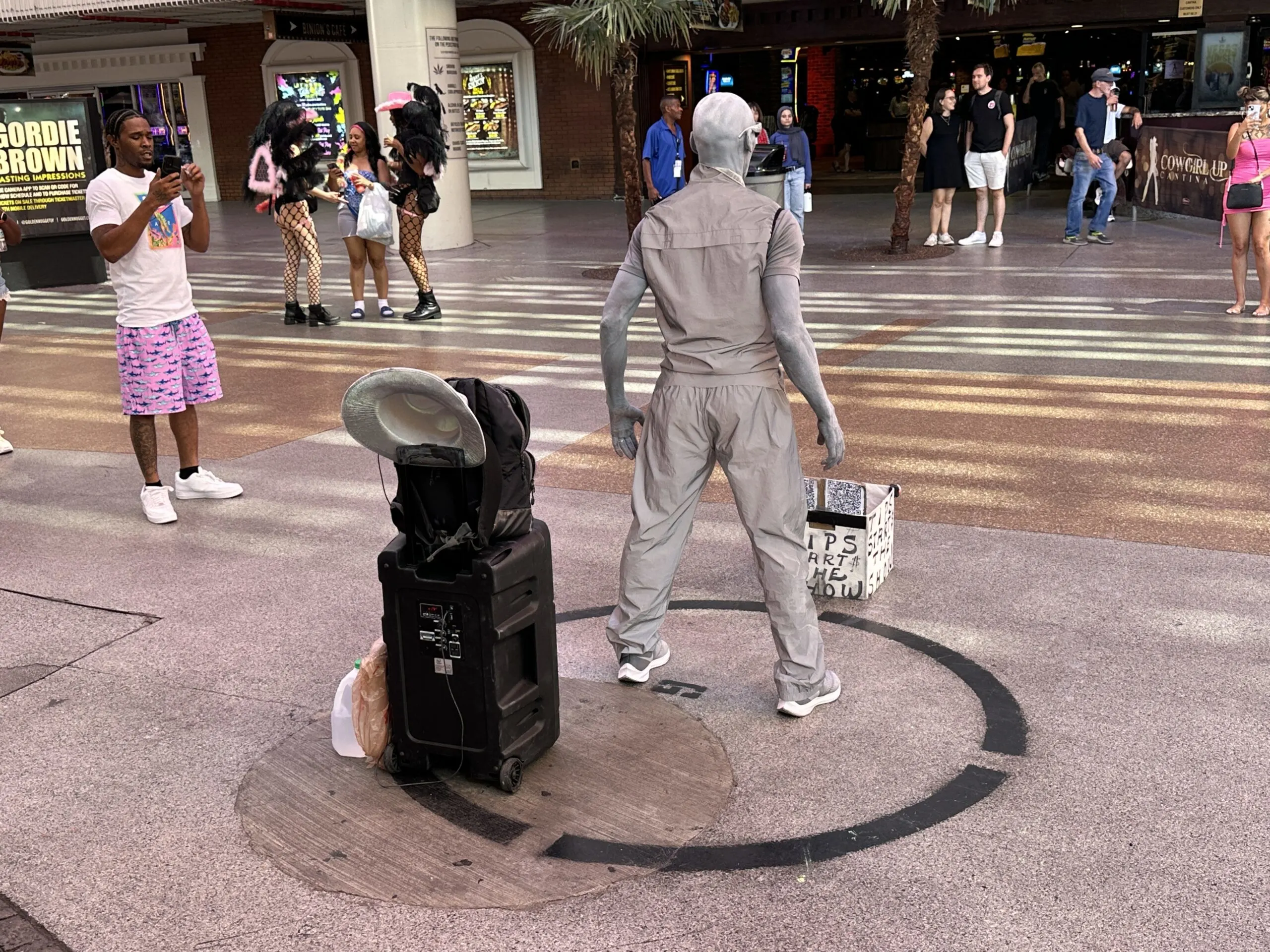 A street perormer dressed in gray and with skin painted in gray poses, waiting for a tip to start the show.