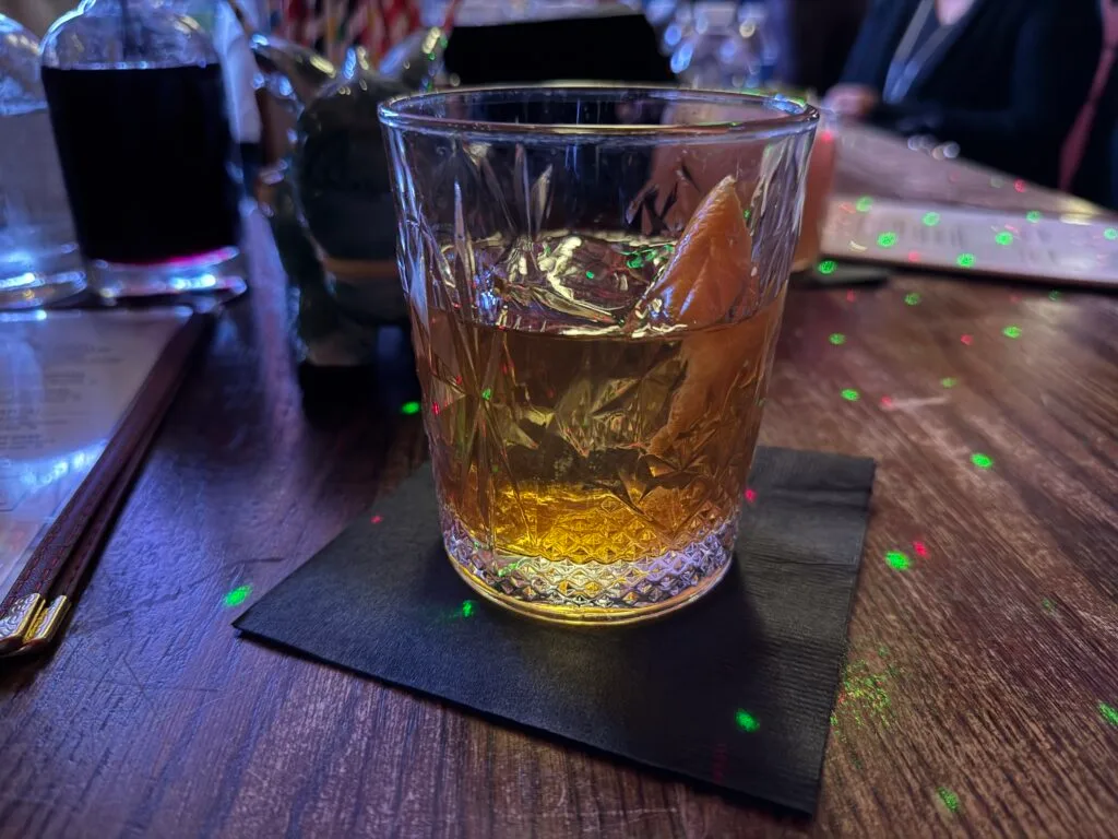 A mezcal old fashioned with a large ice cube and citrus garnish in a glass. 