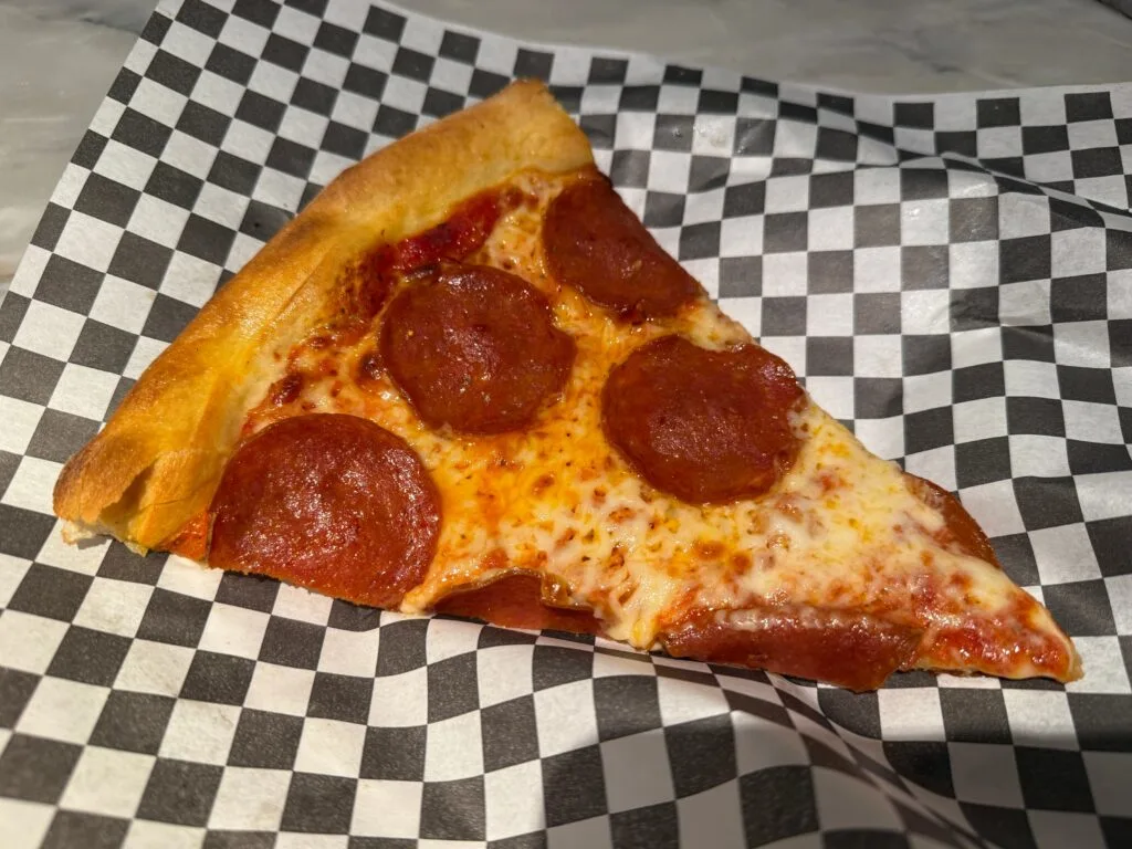 A pepperoni slice of pizza on a checkered paper.