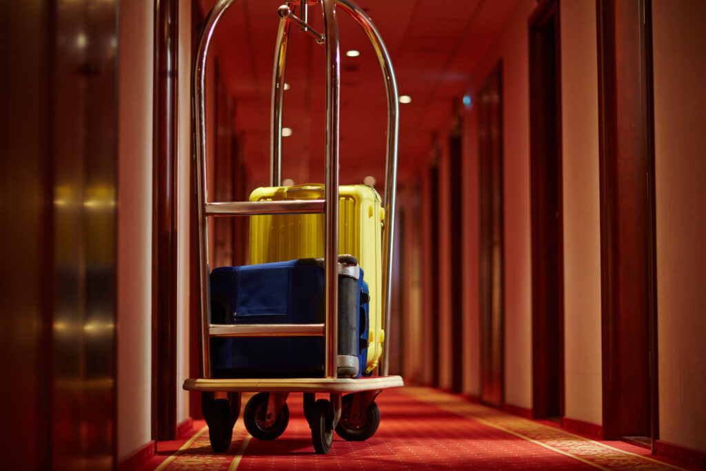 Bellman cart with 2 suitcases on it in a hotel hallway. 