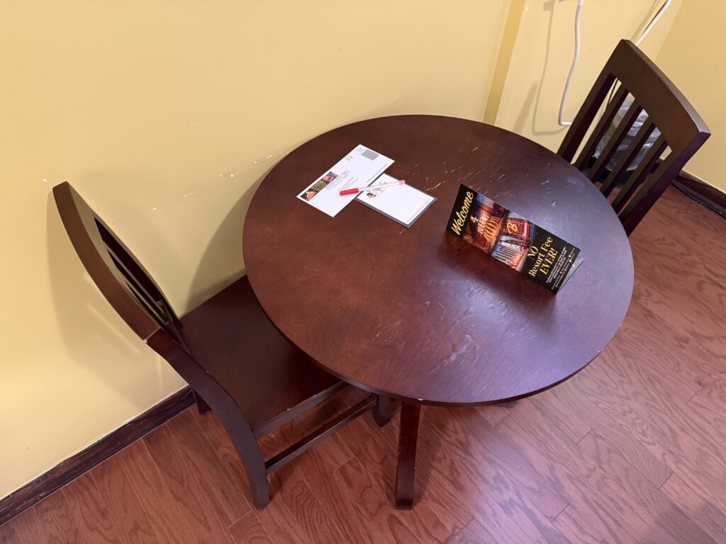 A round wooden table with 2 wooden chairs. The top has water damage. 