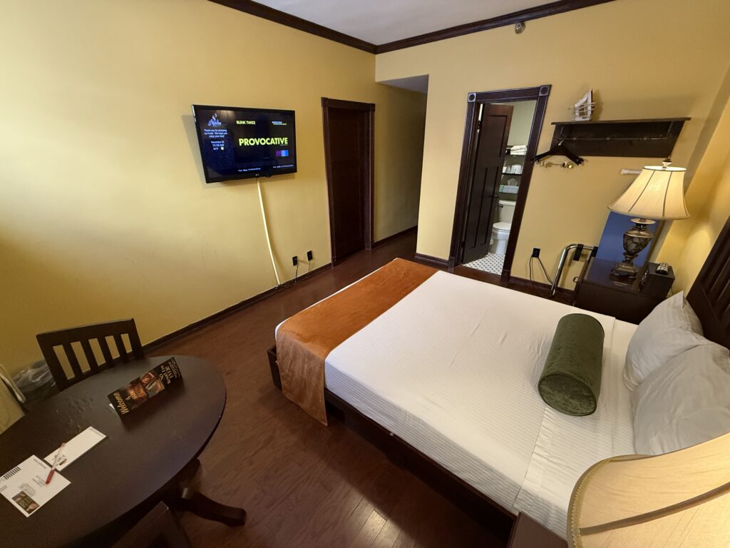 A wide angle of the room, with a small TV hanging on the wall across from the foot of the king bed. 