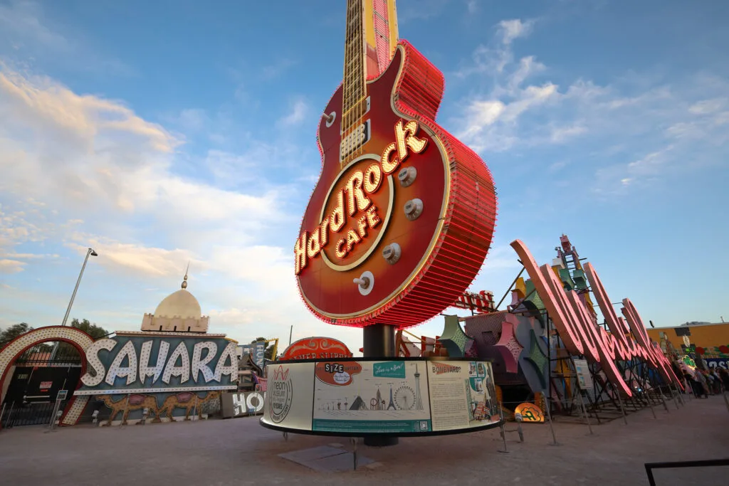 A large Hard Rock Cafe sign in the shape of a guitar is illuminated at dusk. 