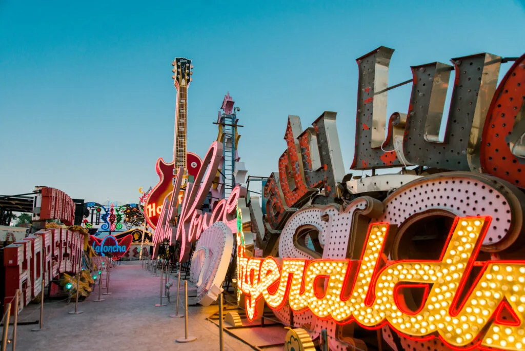 A dirt pathway cut through two walls of vintage signs, some illuminated, some not. 