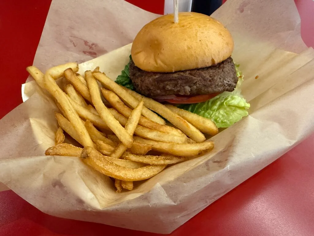 A fat burger alongside french fries in a paper basket.