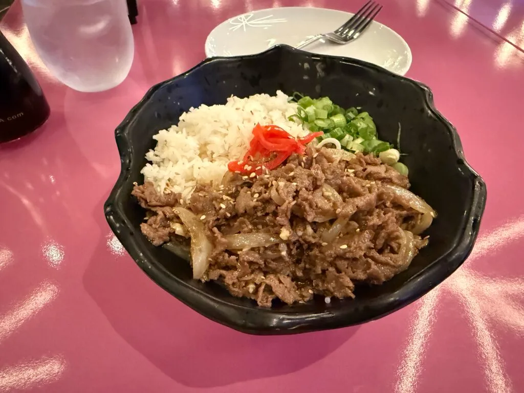 Beef, rice, green onions, and pickled ginger in a black bowl . 