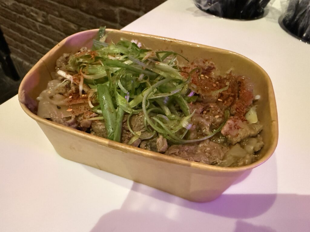 A square shaped bowl with beef, rice, and pickled ginger. 