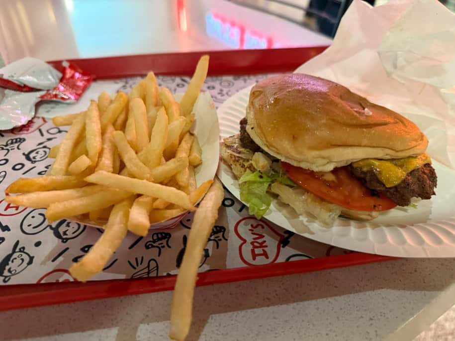 A smash burger on a plate next to a mountain of french fries.