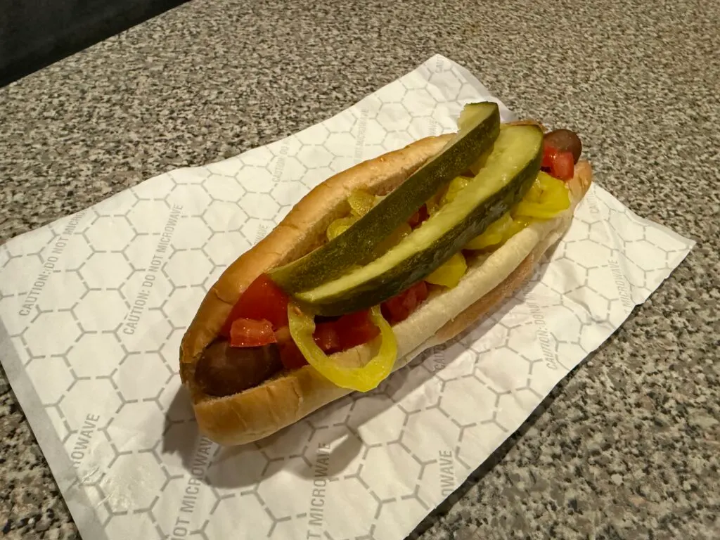 A chicago style hot dog with tomatoes, pickle spears, and peppers piled atop it.