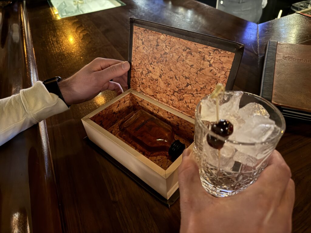 An empty glass with ice, alongside a hollowed out book with a bottle of booze in it.