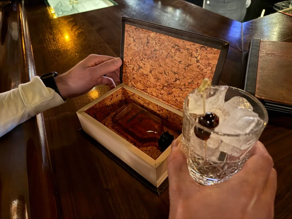 An empty glass with ice, alongside a hollowed out book with a bottle of booze in it.