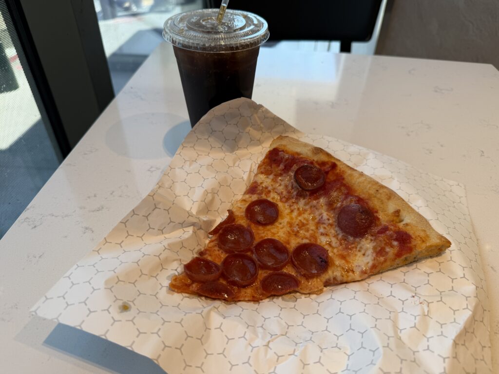 A slice of pepperoni pizza in front of a large soda. 