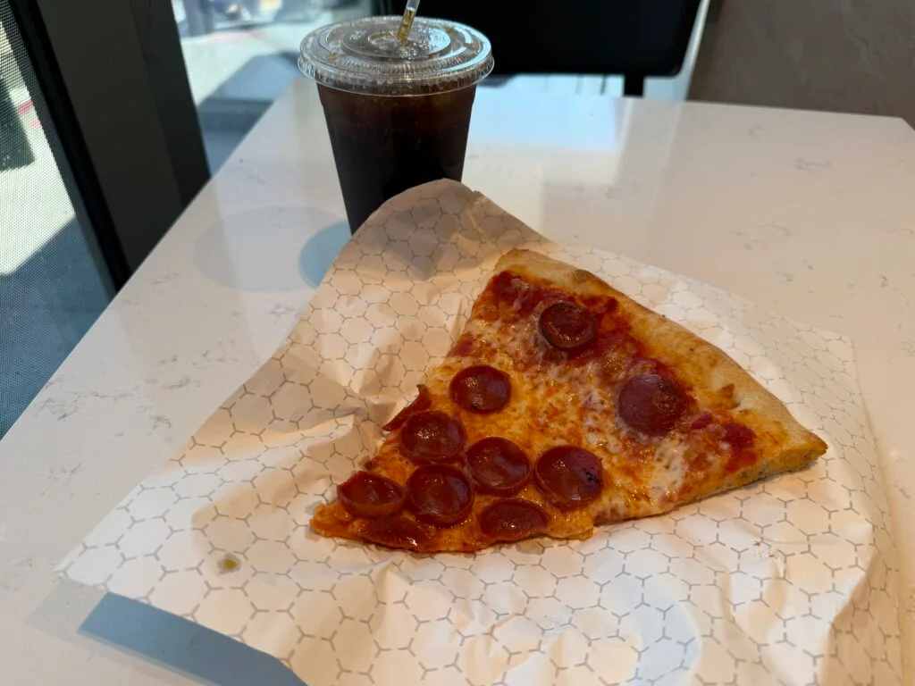A slice of pepperoni pizza in front of a large soda. 