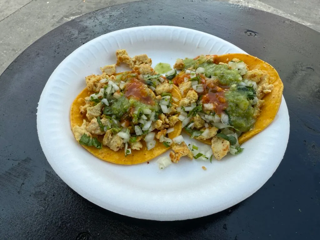 Two chicken tacos on a plate topped with veggies. 