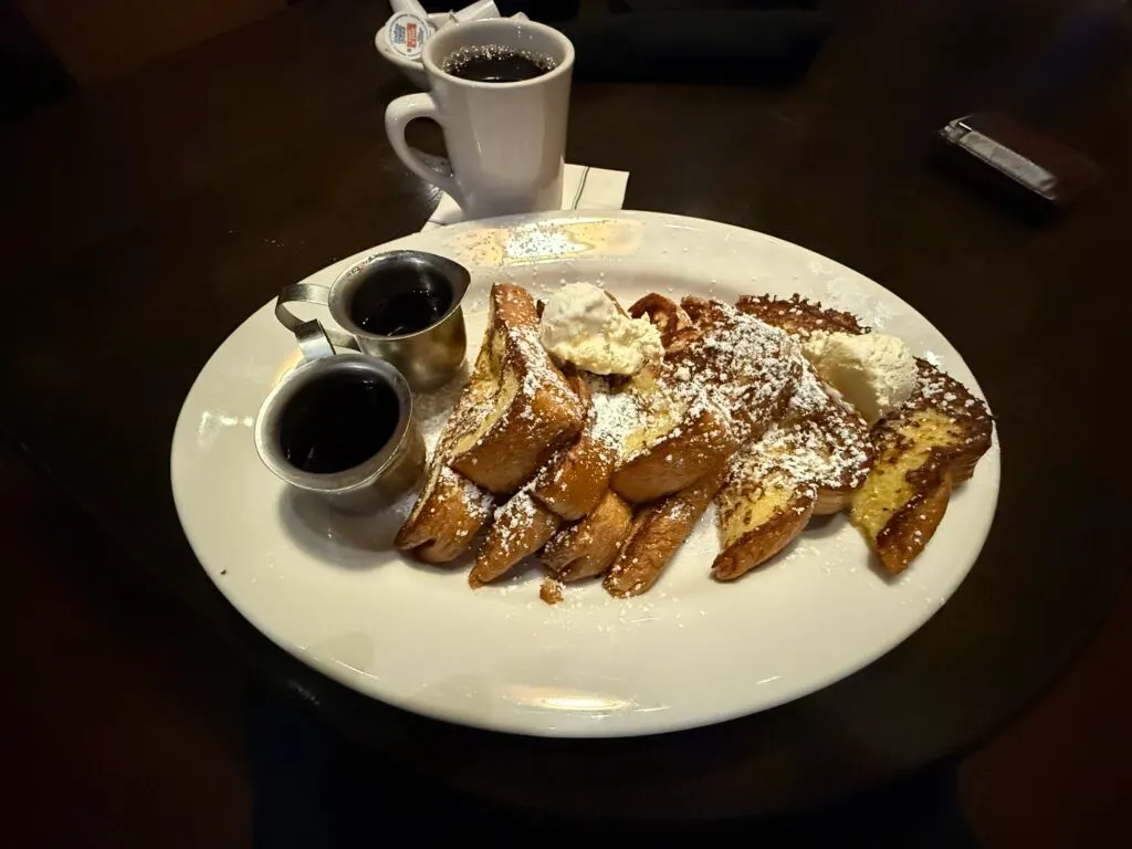 Triangles of french toast laid like fallen dominos across a white plate, topped with powdered sugar. 