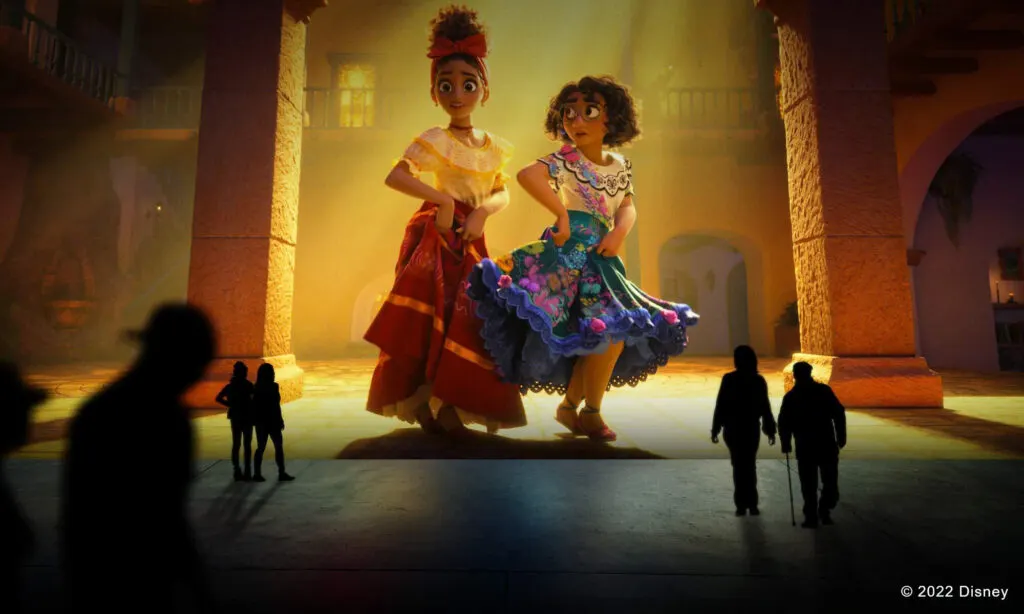 2 characters from a Disney movie are projected onto a massive screen which patrons are silhouetted in front of.