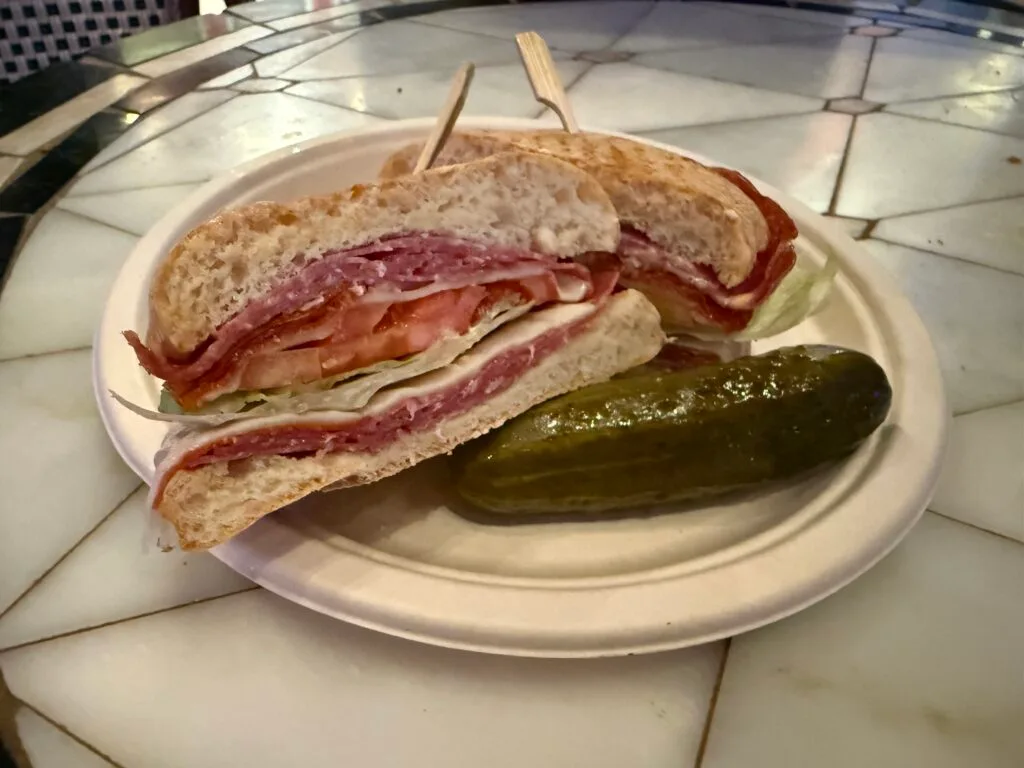 An Italian Stallion, packed with meat and veggies cut in half on a plate with a pickle.