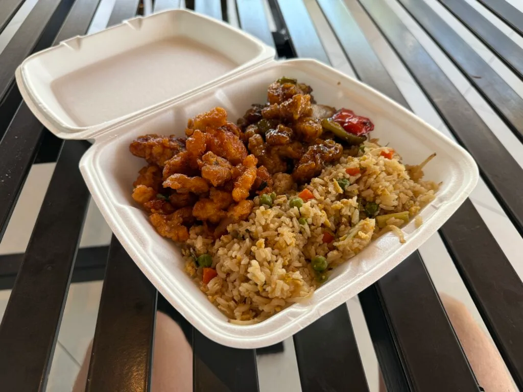 A styrofaom container with 2 types of chicen and fried rice in it. 