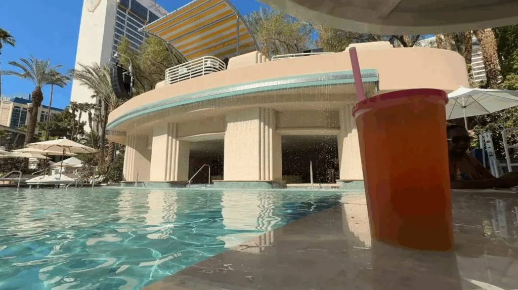 Flamingo's new pool with a rain curtain in the background, and a cocktail in a cup sitting on the bartop in the foreground. 