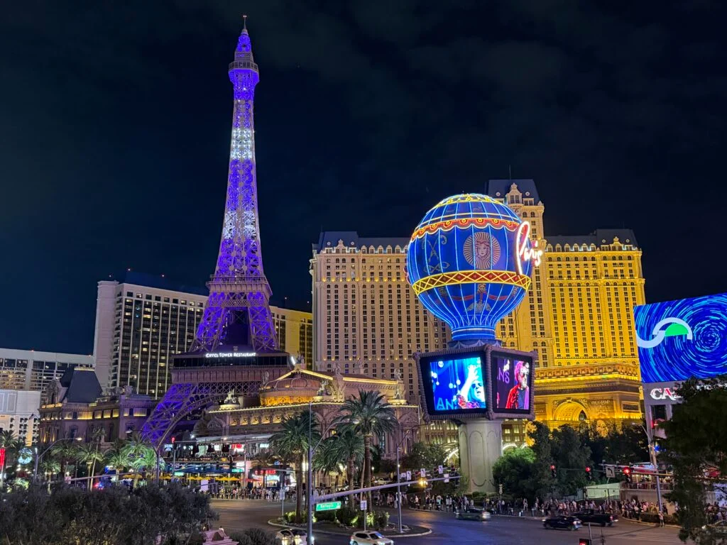 Exterior of Paris Las Vegas at night, and the Eiffel Tower is illuminated in purple and white.