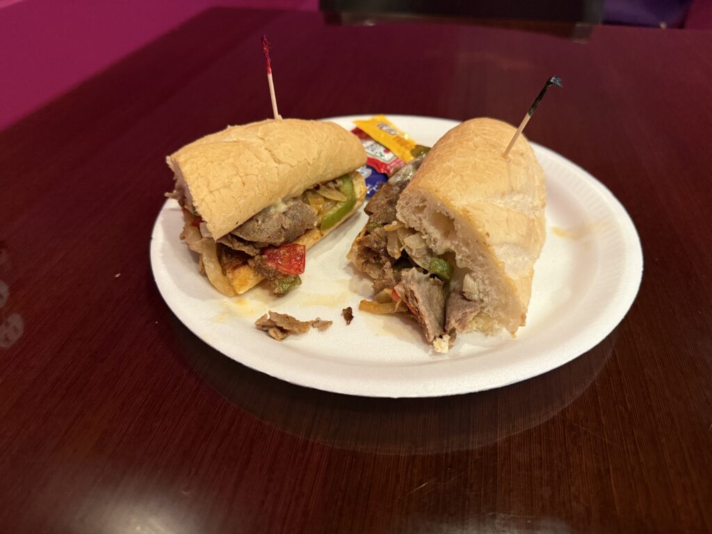 A philly on a hoagie, cut in half on a white syrofoam plate. 
