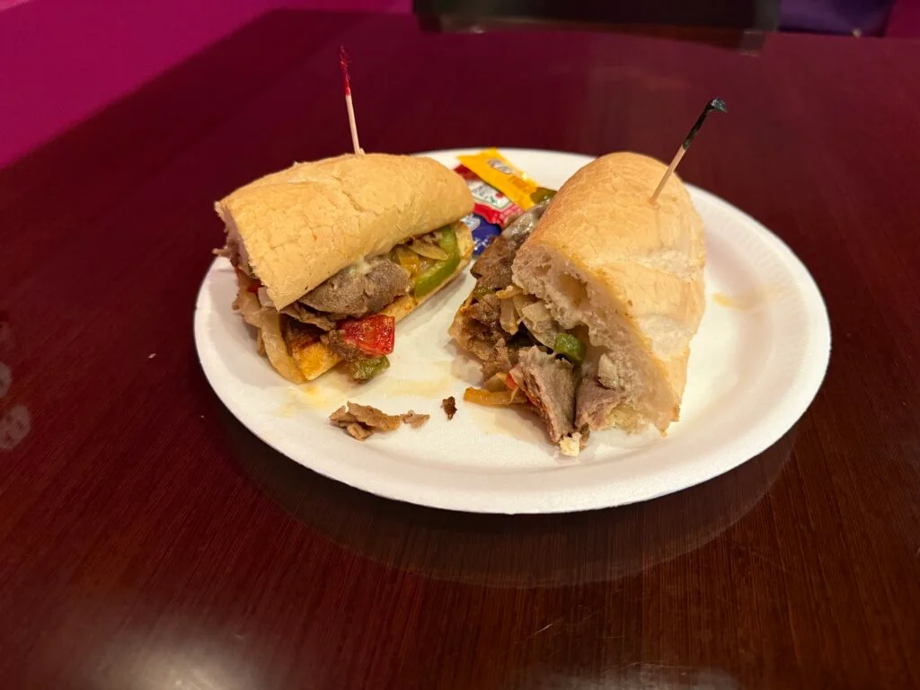 A philly on a hoagie, cut in half on a white syrofoam plate.