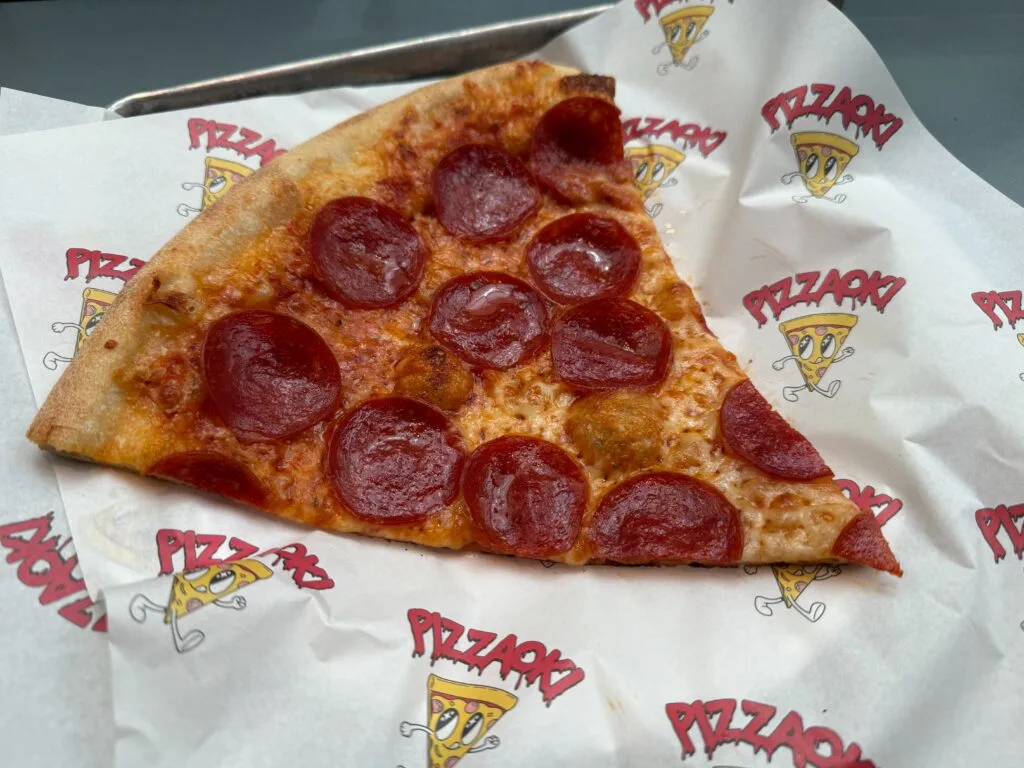 A visibly greasy slice of pepperoni pizza on a tray.