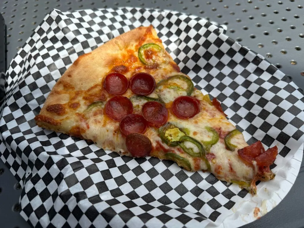 A slice of pizza topped with pepperoni and jalapenos on a checkered paper. 