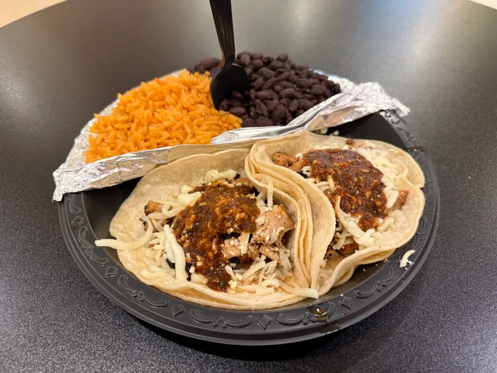 A loaded plate with 2 salsa topped tacos, rice, and black beans. 
