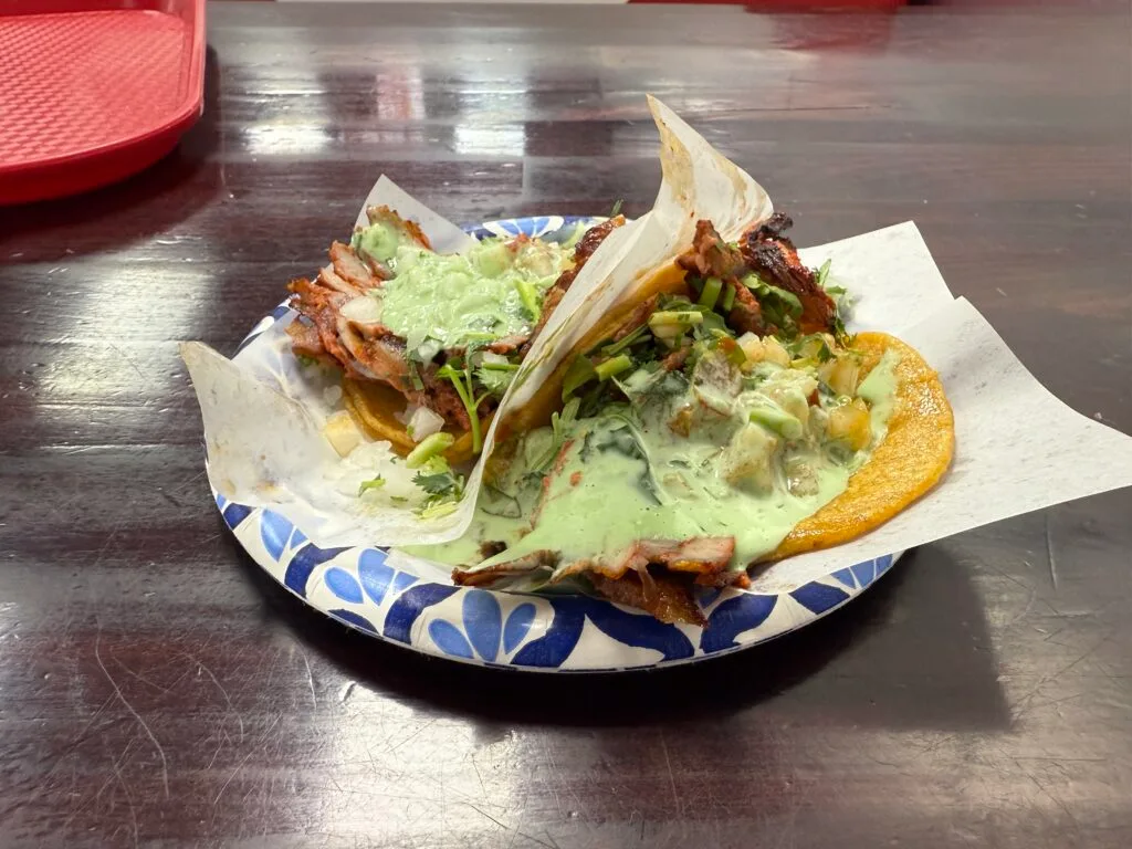 2 adobada tacos on a plate, smothered in a runny guac. 