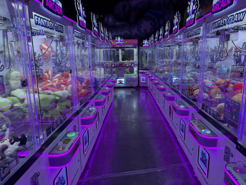 Rows of illuminated claw machines on either side of an isle extend into the distance.