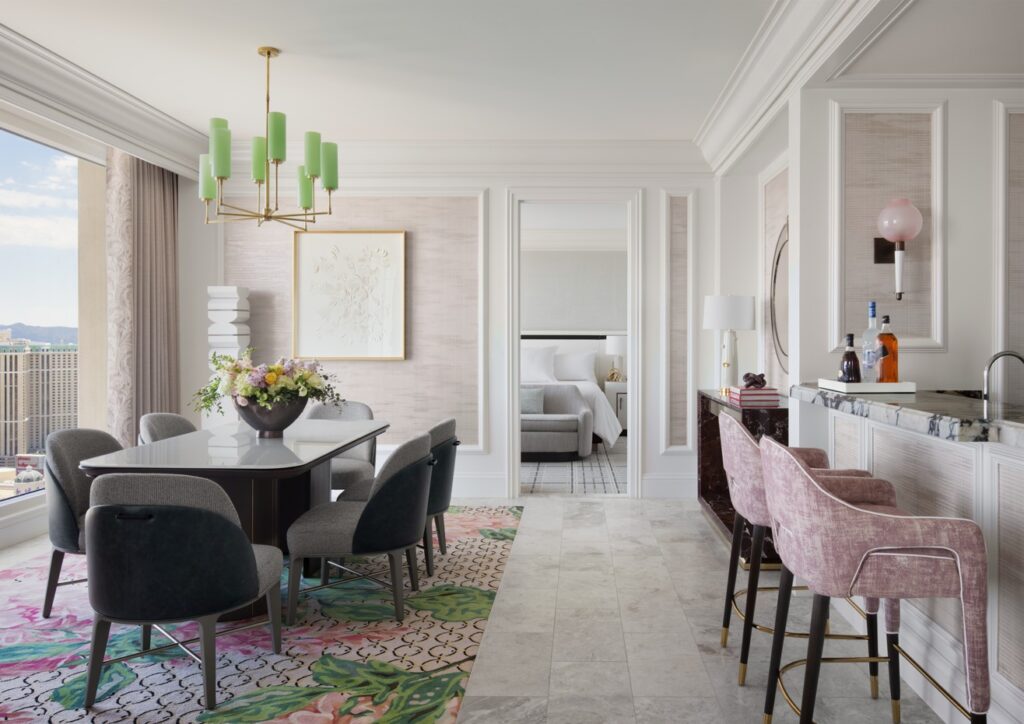 A dining room table on the left and wet bar with stools to the right in a light colored suite.