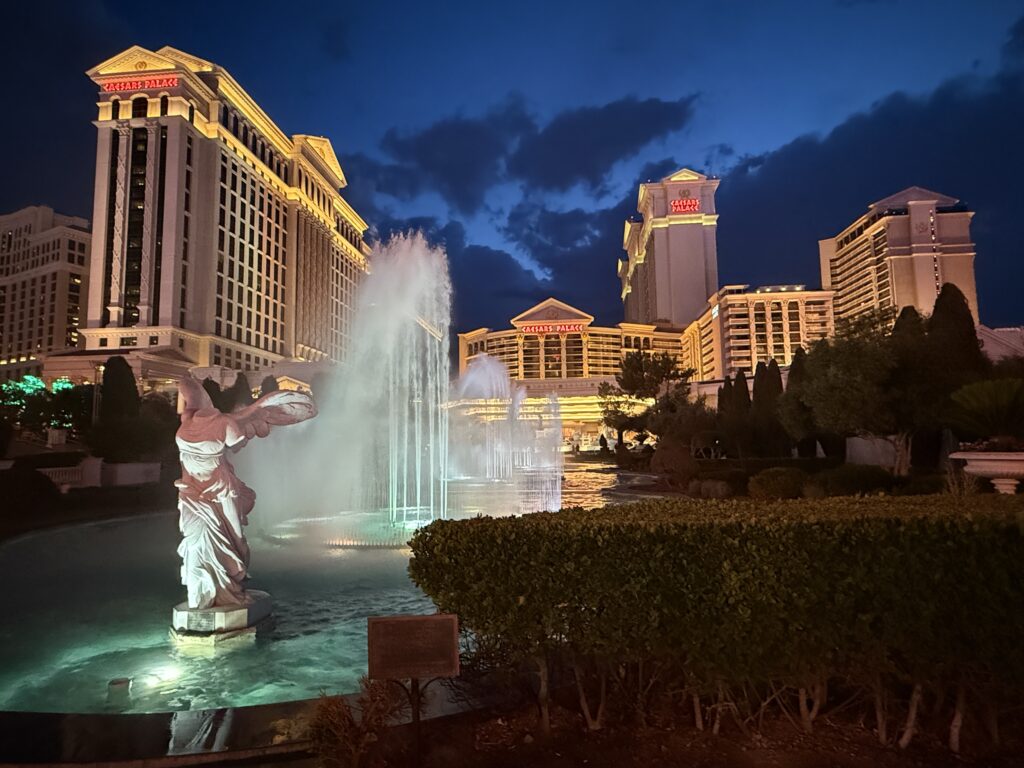Exterior of Caesars at night, with the fountains in the foreground illuminated.