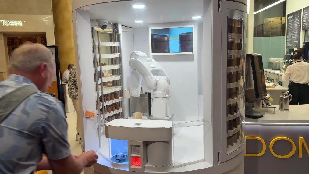 A robotic arm inside a glass enclosed machine makes a cookie shot.
