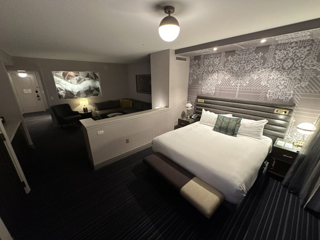A king bed, with a living area over a partial wall in the background.