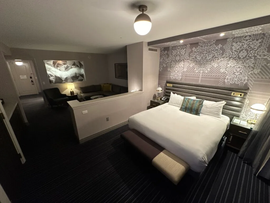 A king bed, with a living area over a partial wall in the background.
