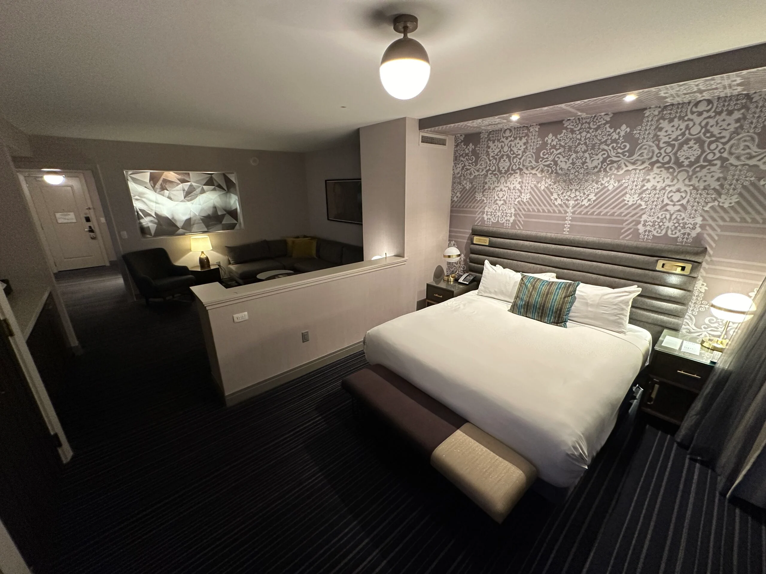 A king bed, with a living area over a partial wall in the background. 