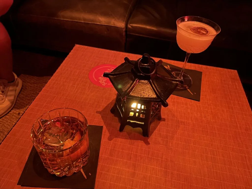 The Patriot and Kiku drinks on at table at the speakeasy with an illuminated centerpiece in the middle of the table