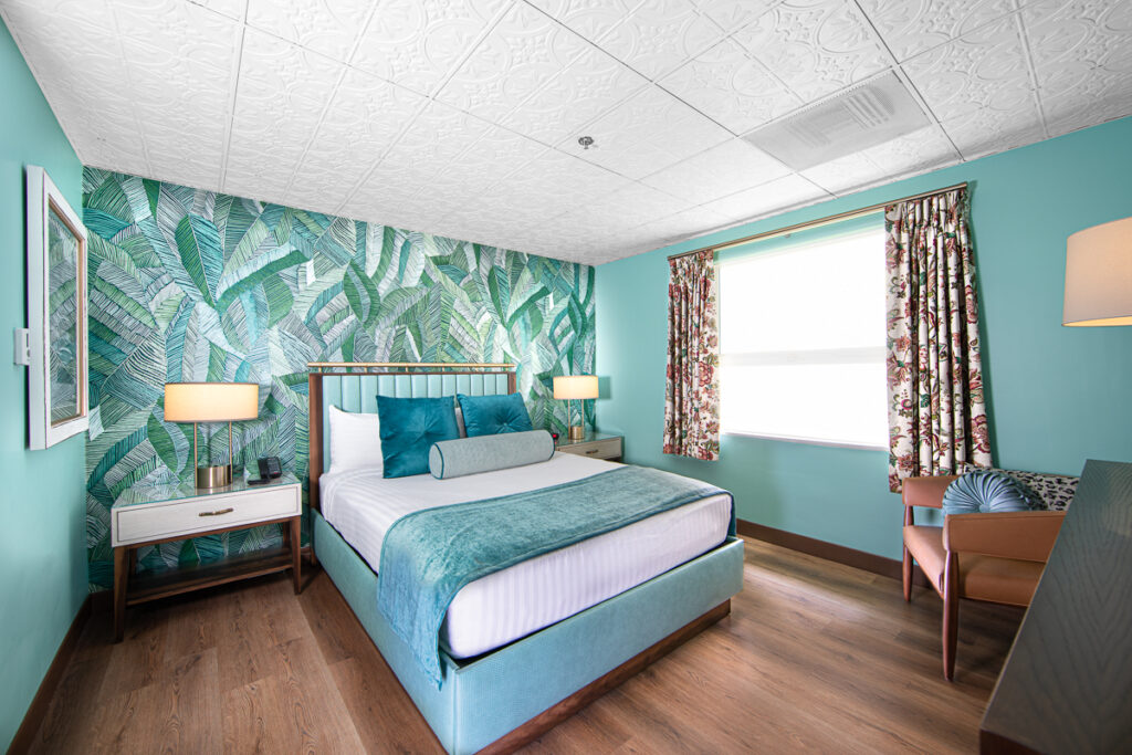 A room with one king bed, mint green walls and accent floral wall. 