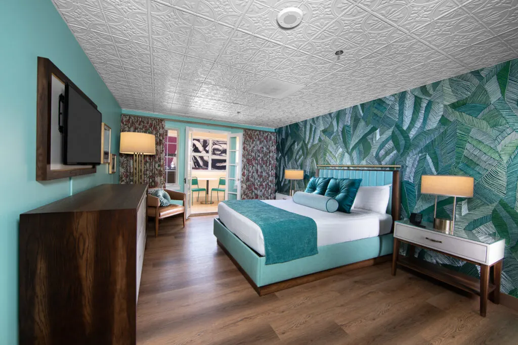 A room at El cortez with mint green walls, a floral accent wall, one king bed, and dark brown flooring.
