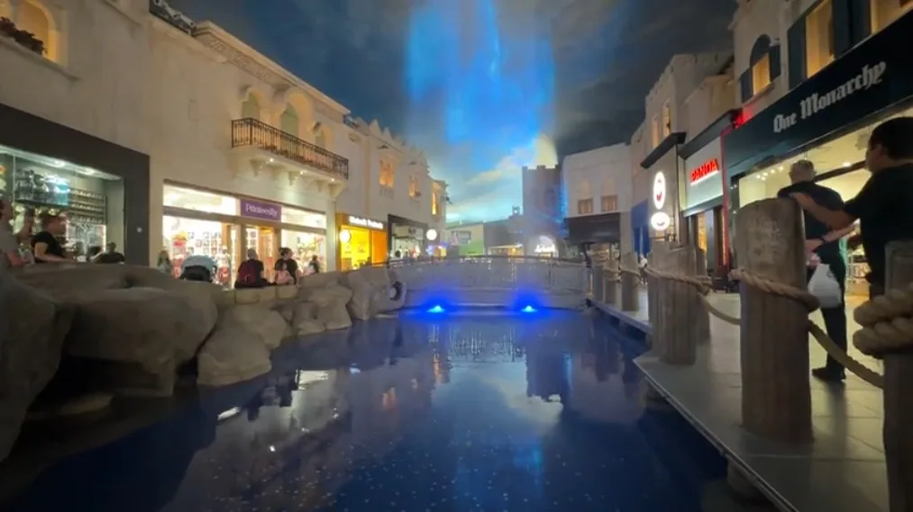 A pond, with a waterfall falling from the ceiling. An image is projected onto the falling water. 