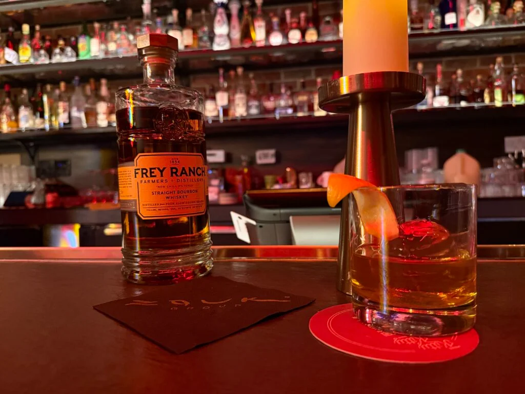 A bottle of bourbon next to a cocktail glass.