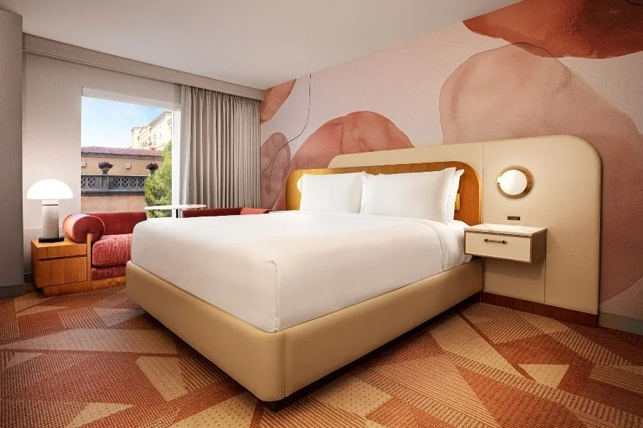MGM's renovated hotel room with a pink floral accent wall, pink couch below the window, and king bed